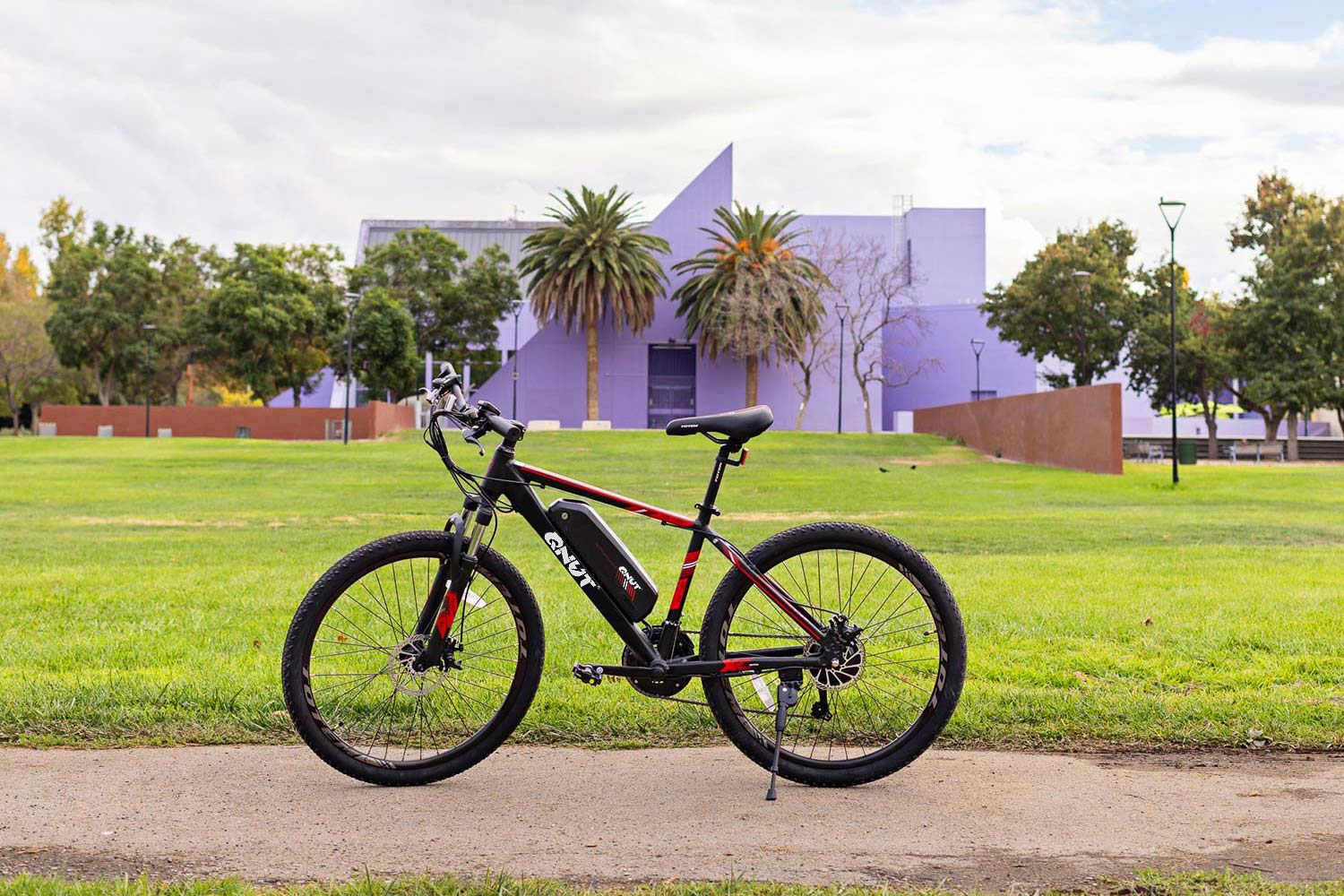A QNUT electric mountain bike is parked on a paved path in a grassy park.